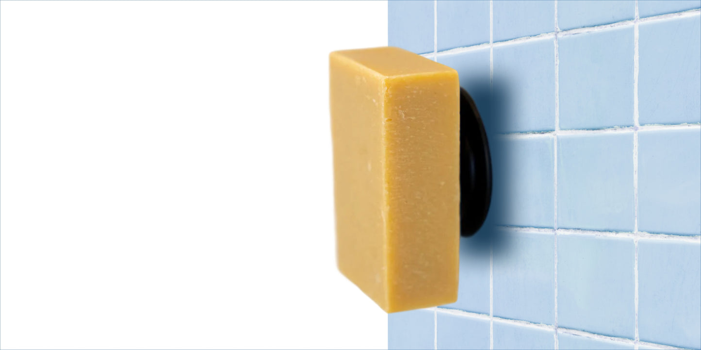 A Lemongrass and Ginger Goodlather soap bar is attached to a blue tiled wall using a black and white Soapi Magnet Holder by Goodlather. The left side background is plain white, adding a modern Canadian touch to your bathroom.