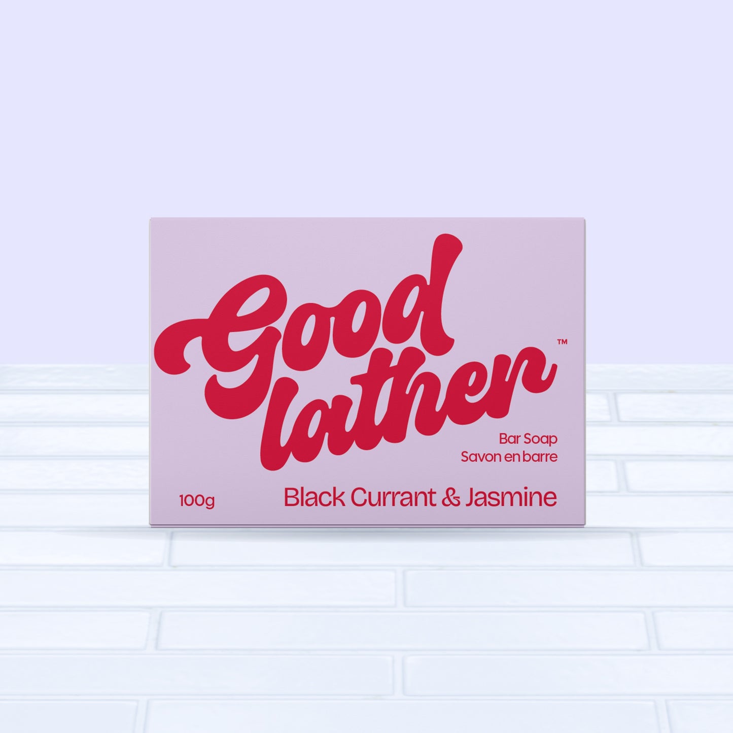 A Goodlather Black Currant and Jasmine Bar Soap in a bold red and pink box rests on light tiles with a pale purple background. This sustainable, all-natural Canadian soap bar weighs 100g.