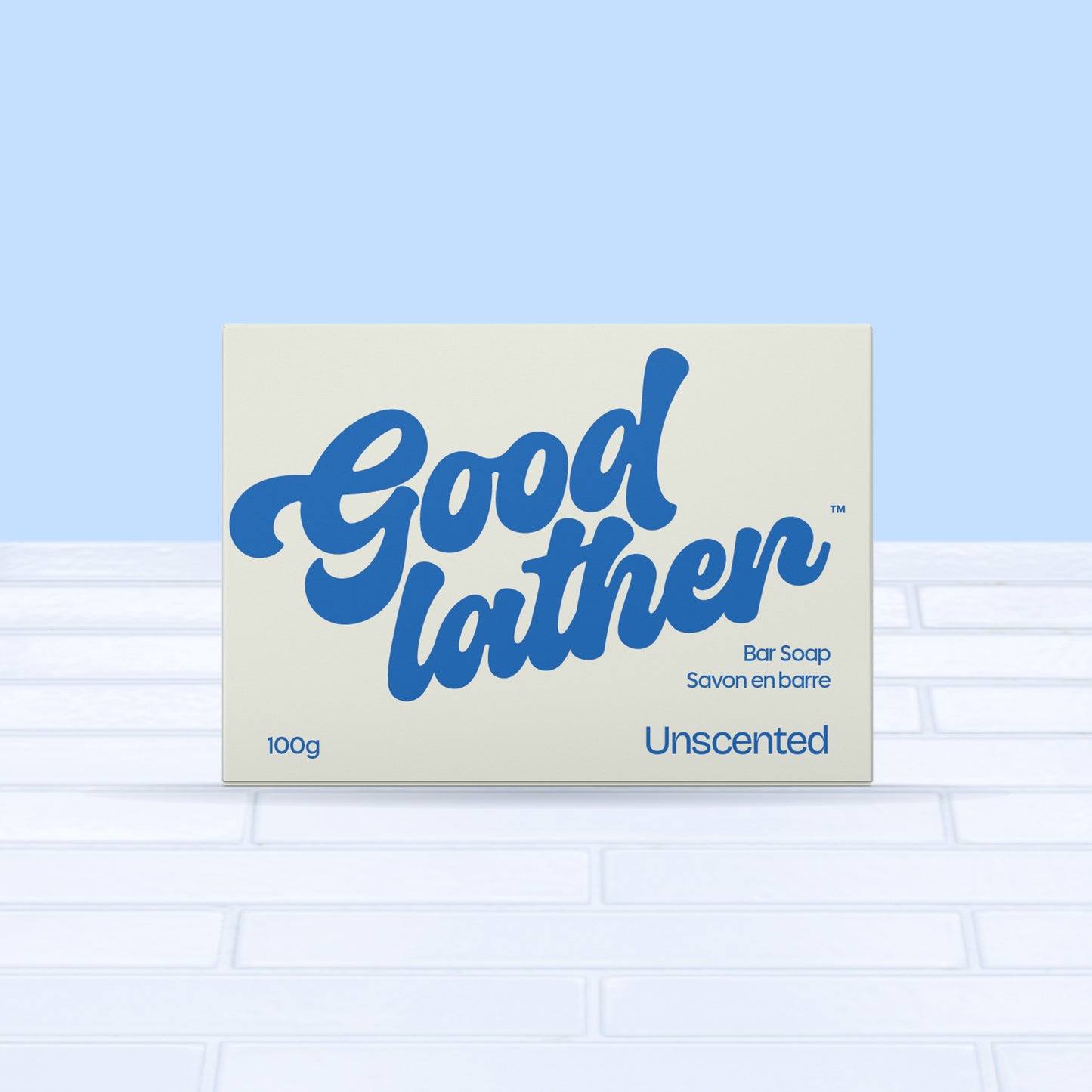 A 100g Goodlather Unscented Soap Bar, featuring bold blue script on a light background, rests on white tiles against a pale blue backdrop—ideal for sensitive skin.