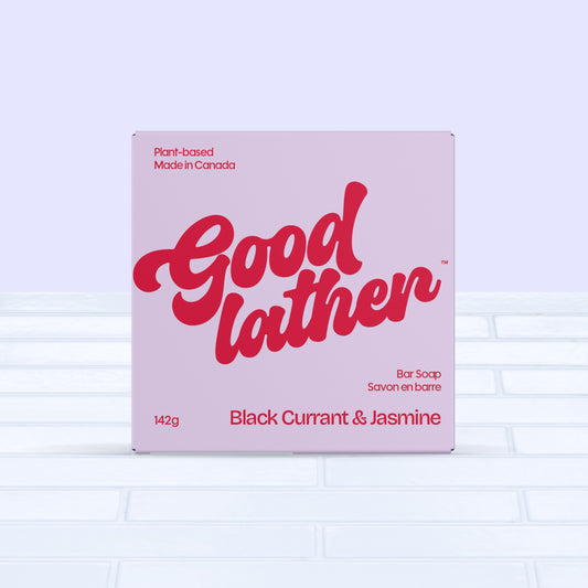 A Goodlather Black Currant and Jasmine Bar Soap in bold red and pink packaging rests on white tiles, highlighting this sustainable, all-natural, and plant-based bar soap made in Canada.