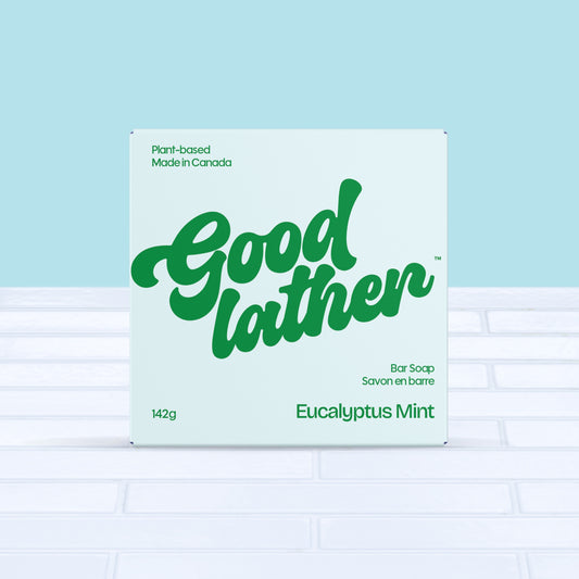 A light blue and green box of Goodlather Eucalyptus Mint Bar Soap (142g) rests on white tiles with a light blue background. The packaging notes its natural ingredients, plant-based formula, and Made in Canada.