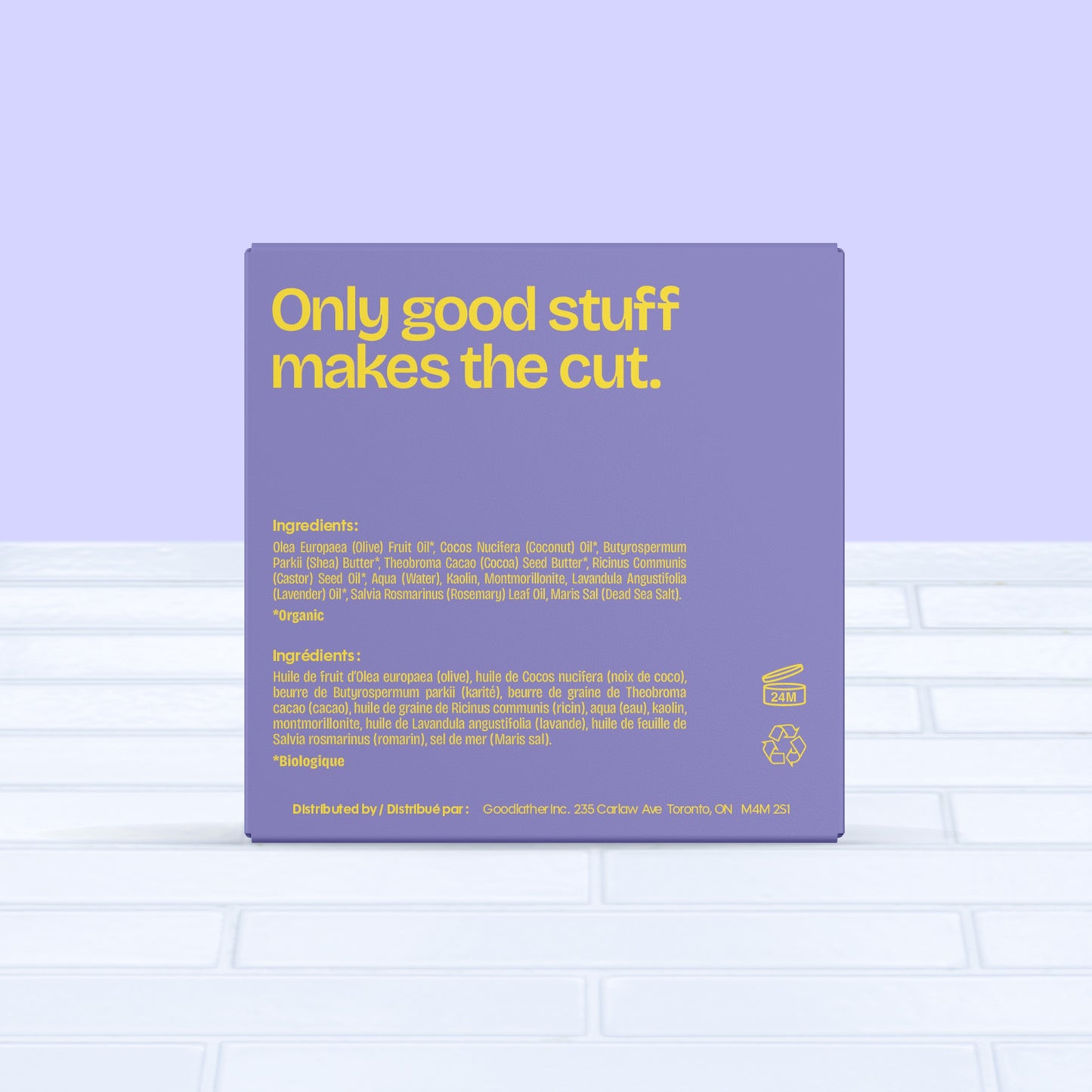 A purple and yellow Goodlather Lavender and Rosemary Bar Soap box reads "Only good stuff makes the cut," with ingredients, eco-friendly info, and distribution details in English and French. Set on white tile against a lavender wall. Made in Canada.