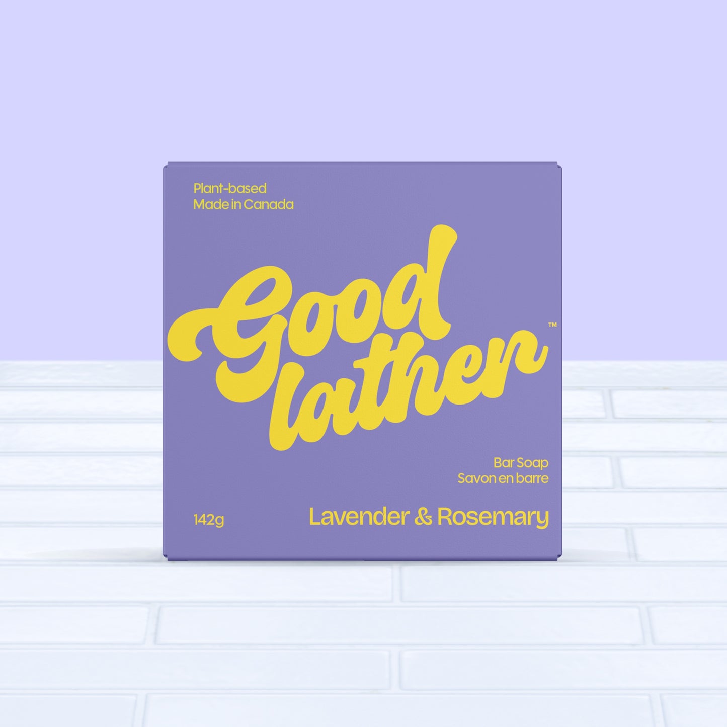 A purple and yellow box of Goodlather Lavender and Rosemary Bar Soap sits on white tiles. The label reads “Plant-based, Made in Canada,” emphasizing this eco-friendly, sustainable 142g product.