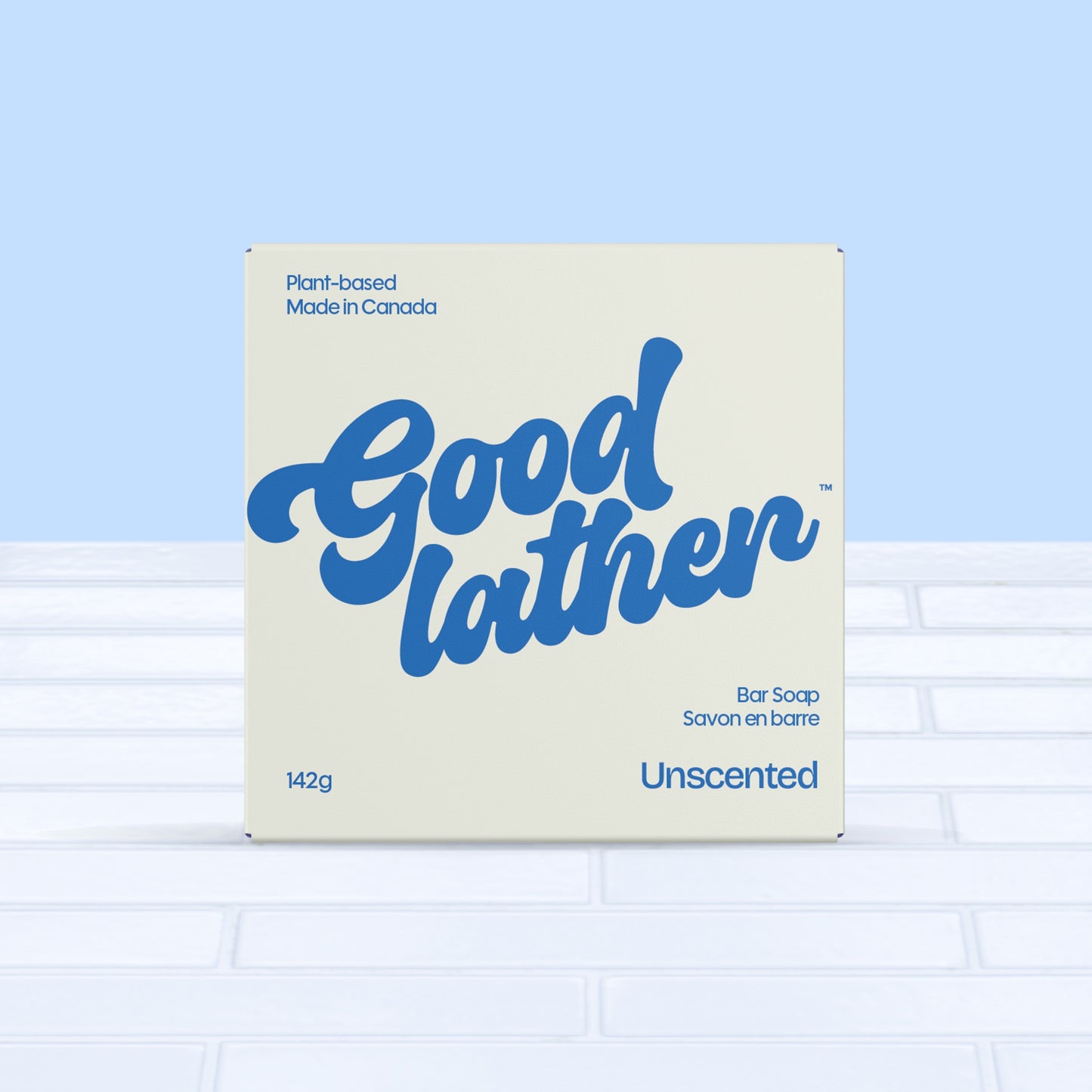 A 142g box of Goodlather Unscented Soap Bar, plant-based and made in Canada with natural ingredients, rests on white tiles against a pale blue background. The cream packaging displays bold blue lettering.